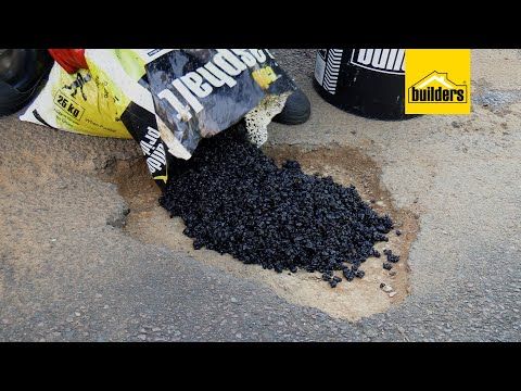 Person pouring black asphalt from a bag to fill a pothole in a road.
