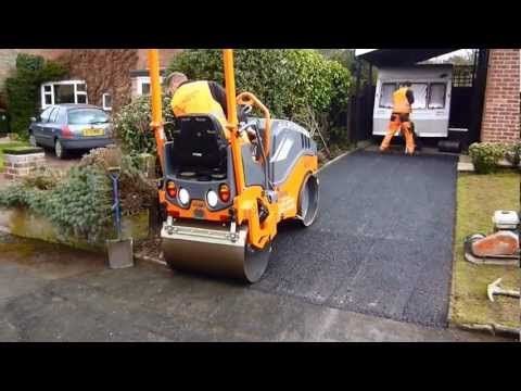 Orange road roller compacting asphalt driveway; two workers nearby.