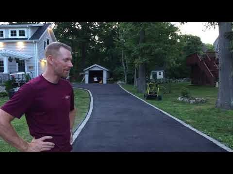 Man stands by newly paved driveway, looking towards a garage and trees in the background.
