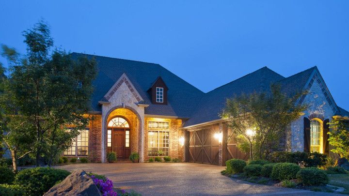 Upscale brick home at dusk with lights illuminating the front door, windows, and driveway.
