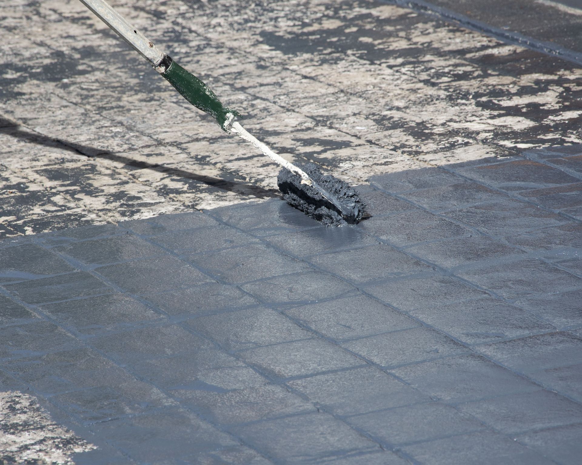 Person applying a dark coating to a flat, tiled roof with a roller.