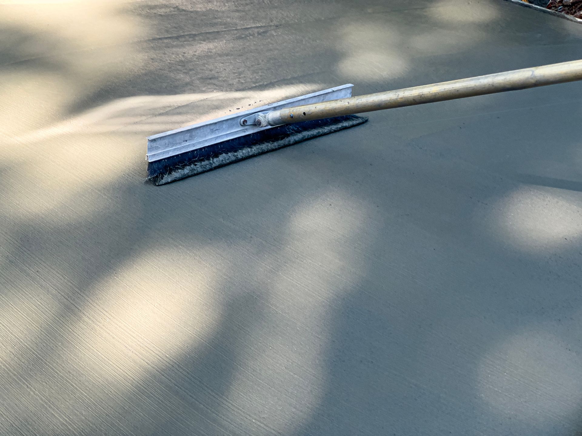 Person using a broom to finish a newly poured concrete surface outdoors.