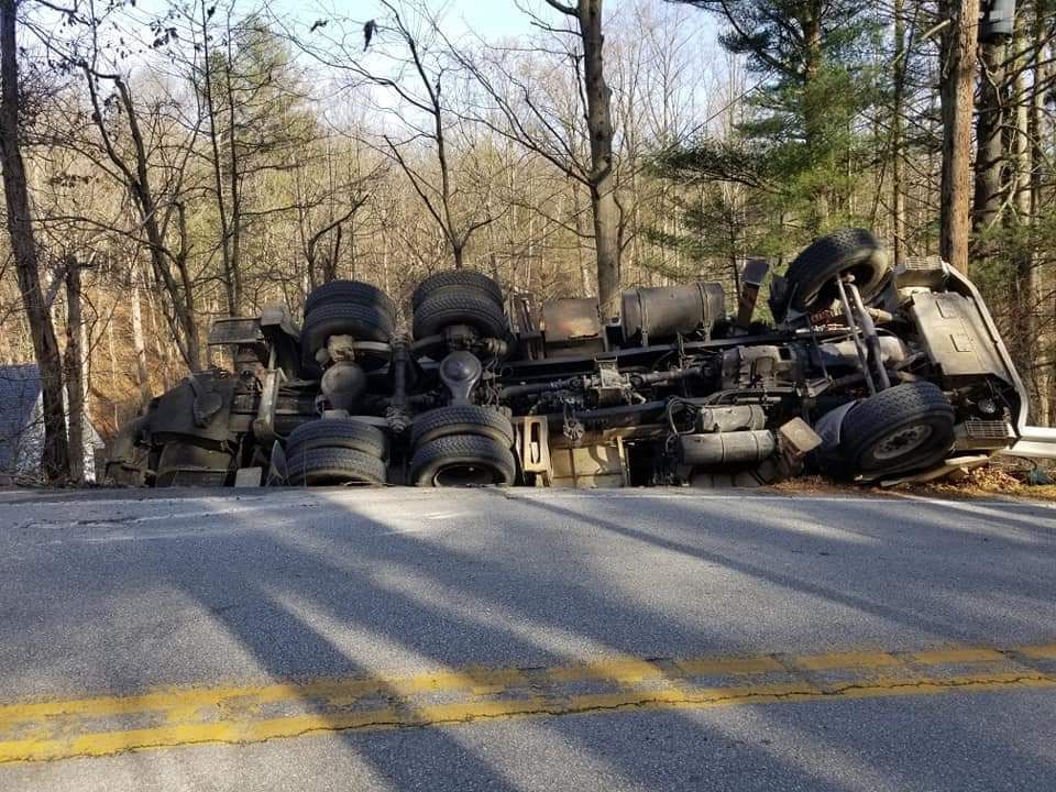 A semi truck is turned over on the side of the road.