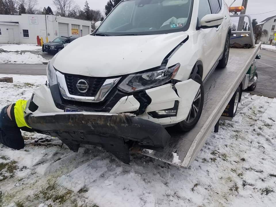 A white nissan rogue is being towed by a tow truck in the snow.