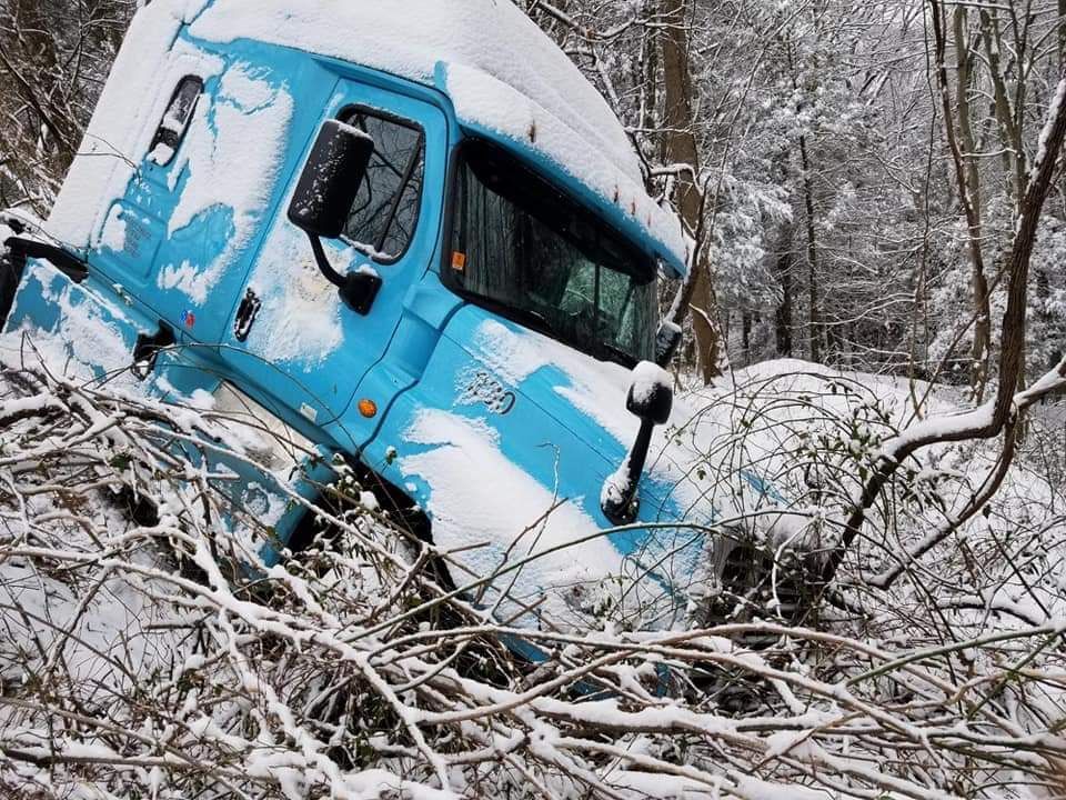 A blue truck is stuck in the snow in the woods.