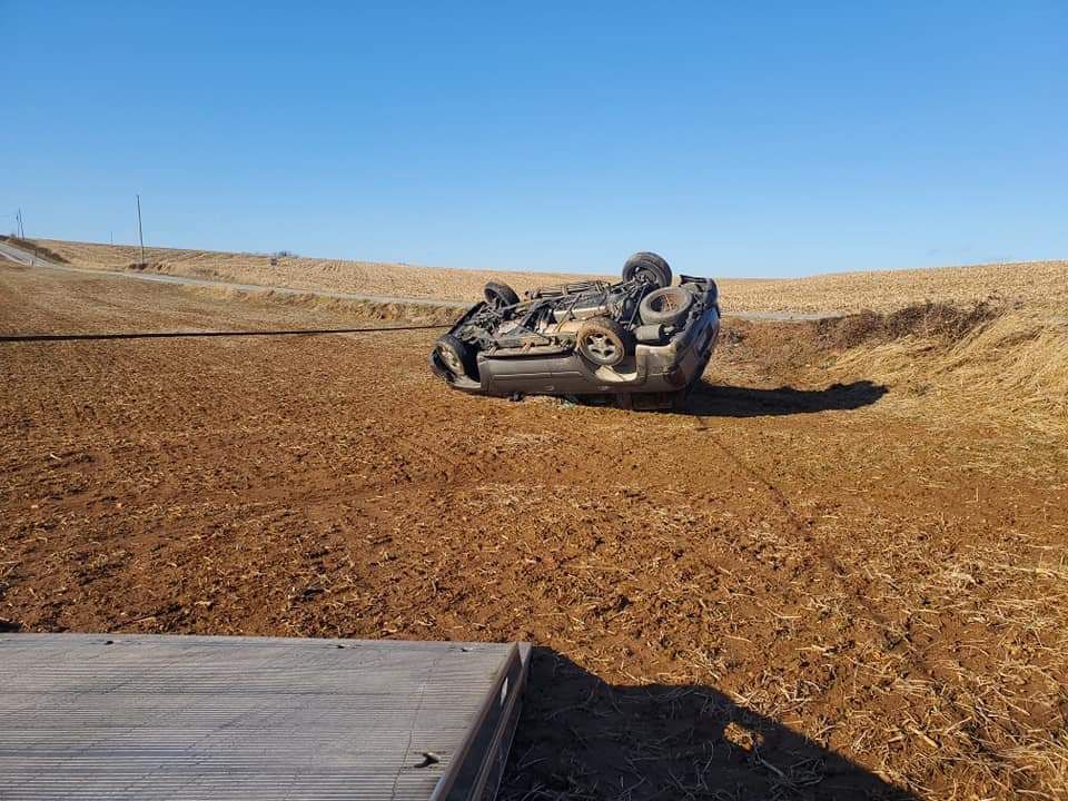 A car is upside down in the middle of a field.