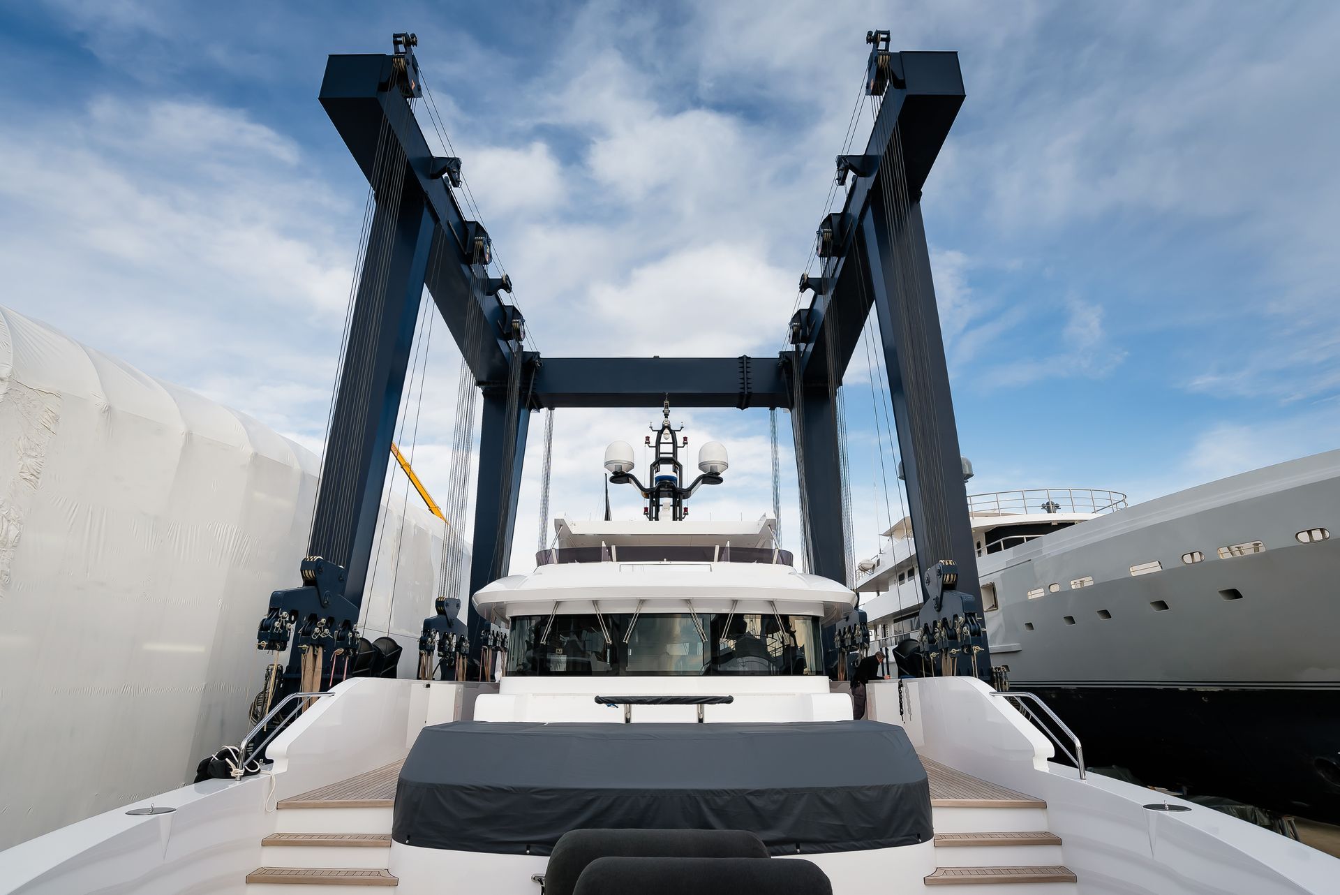 A large yacht positioned under a massive crane; blue sky, white clouds.