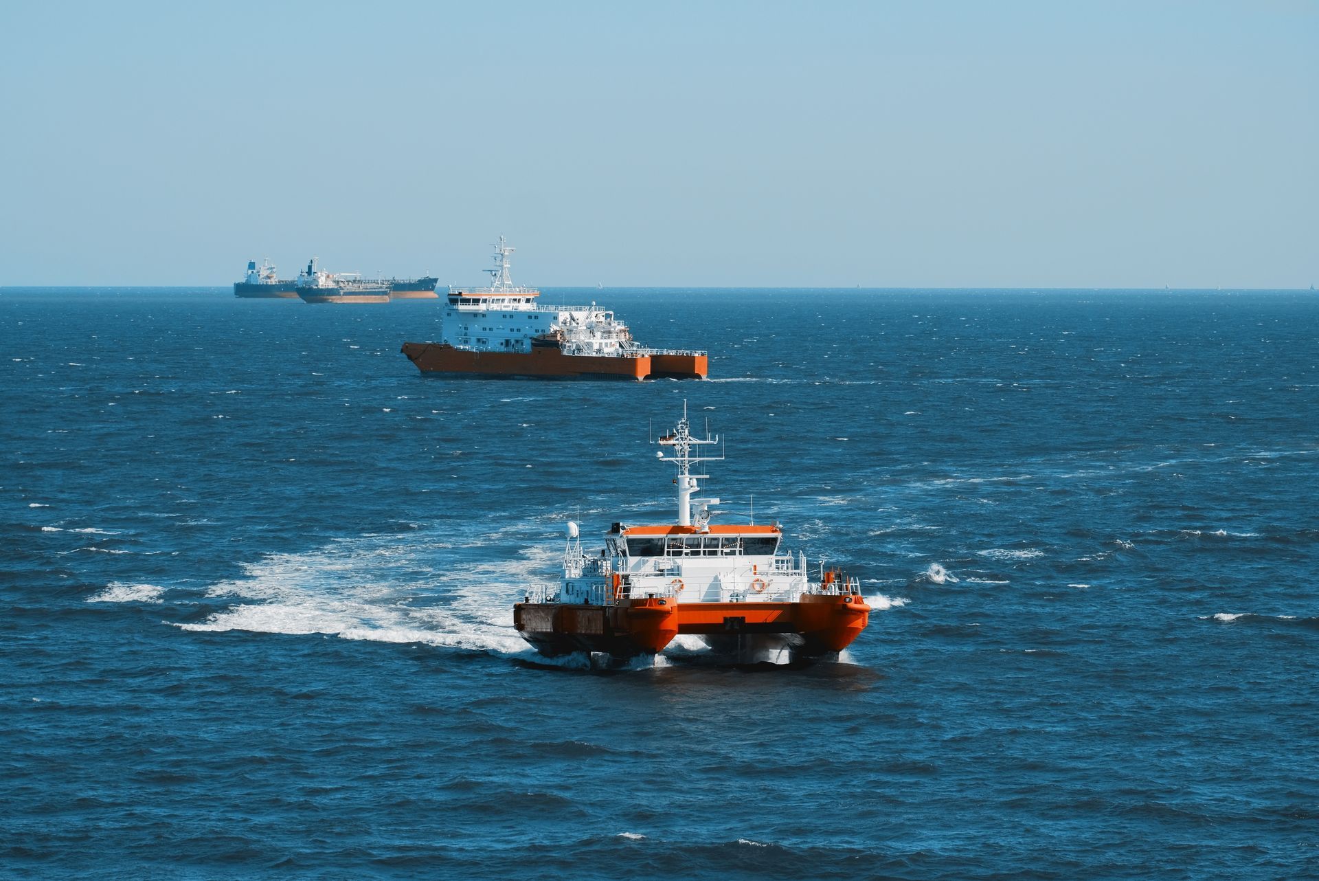 Orange and white boats on blue water, a clear sky, and other ships visible in the distance.