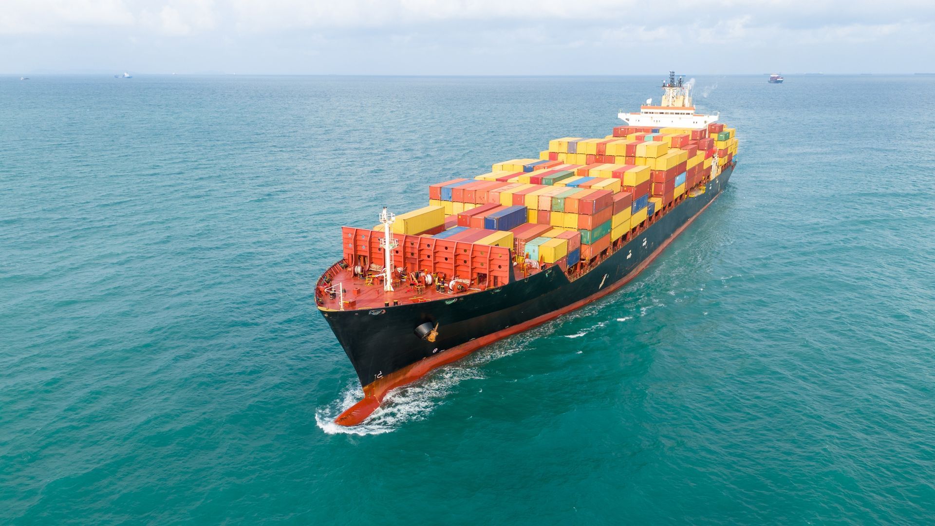 Large cargo ship sailing on blue ocean, carrying colorful shipping containers.
