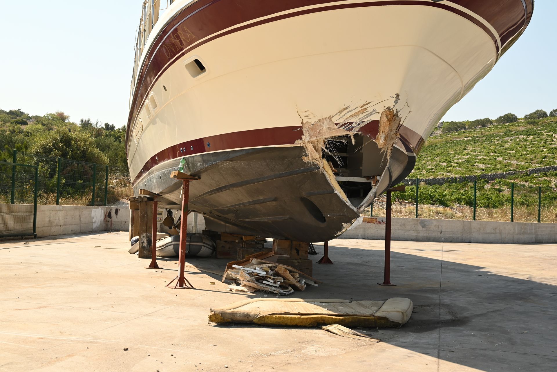 Damaged boat on stands in a concrete lot, with a hole in the hull.