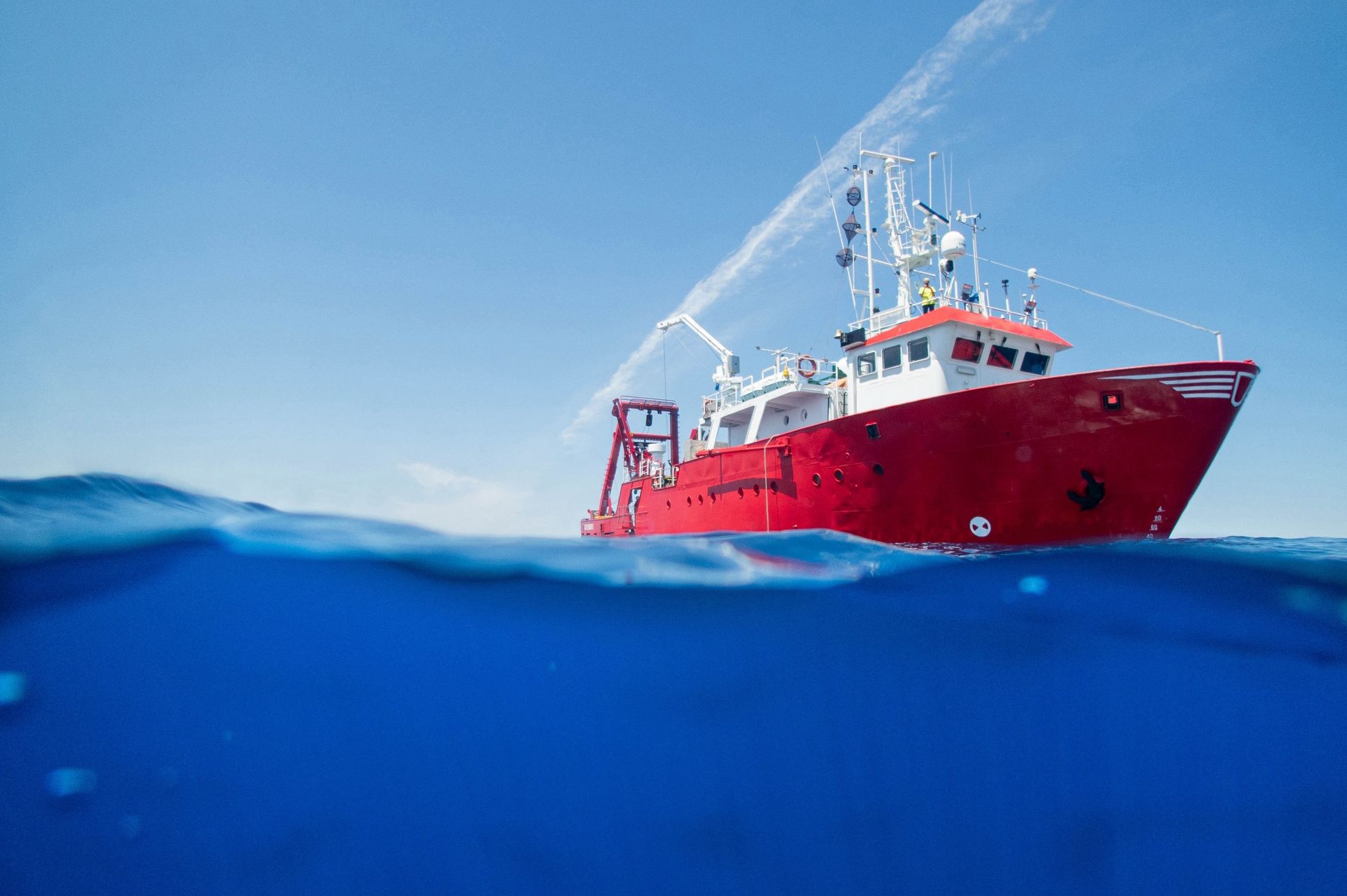 Red research vessel sprays water, blue sea, clear sky.