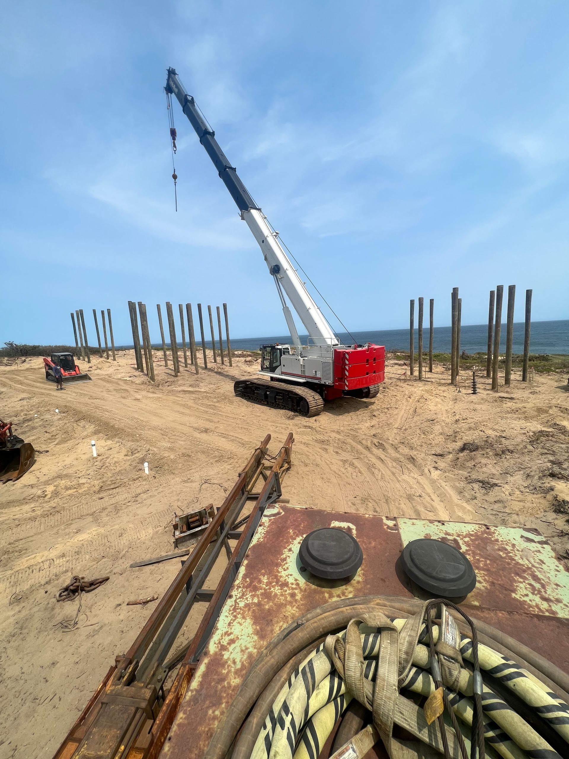 A red and white crane on a barge works near a rocky shoreline, dumping material into the turquoise water.