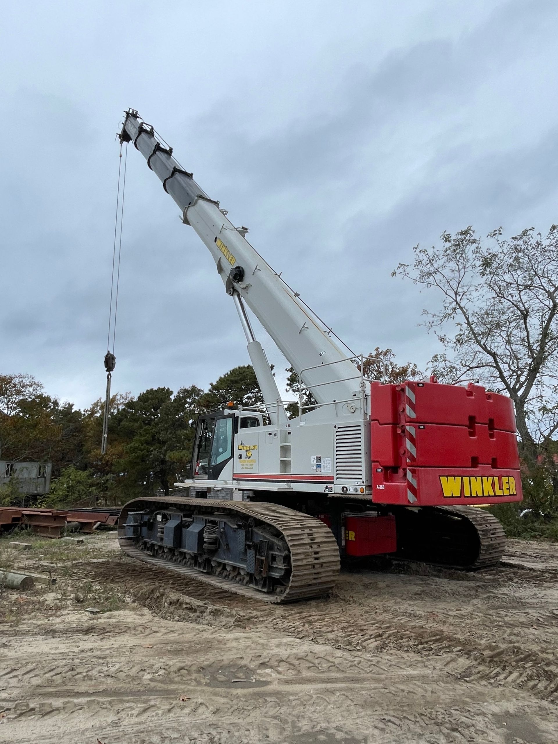A large yellow mobile crane stands at a construction site with exposed concrete columns and steel framework at dusk.