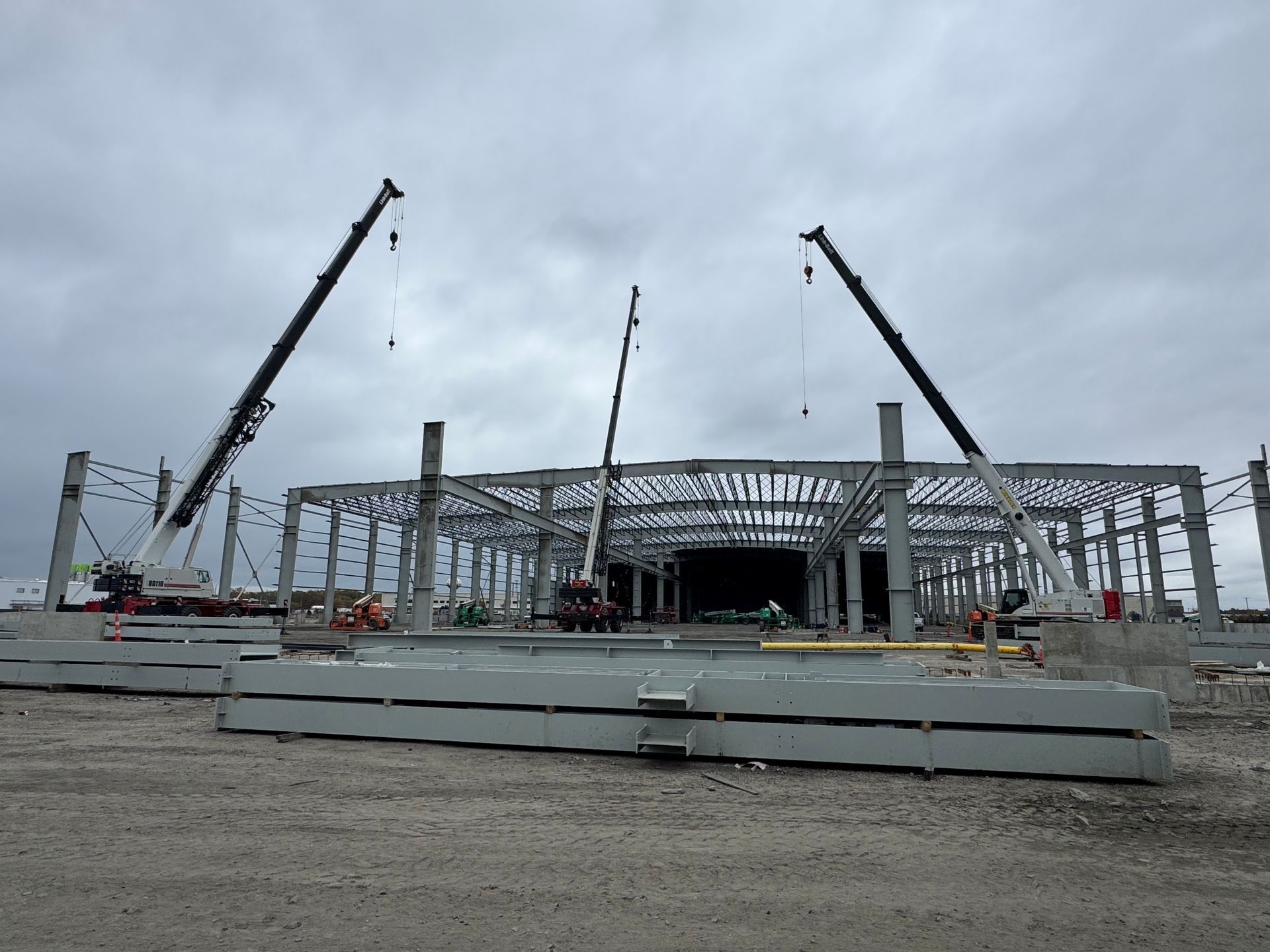 A yellow mobile crane parked on gravel with lush green trees in the background.