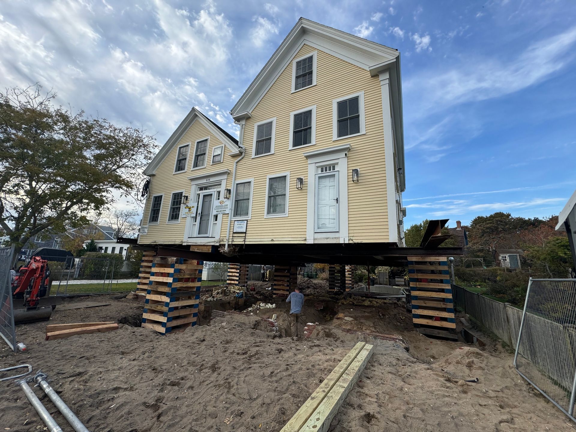 A bright yellow mobile crane parked on a paved lot with large industrial storage tanks in the background.