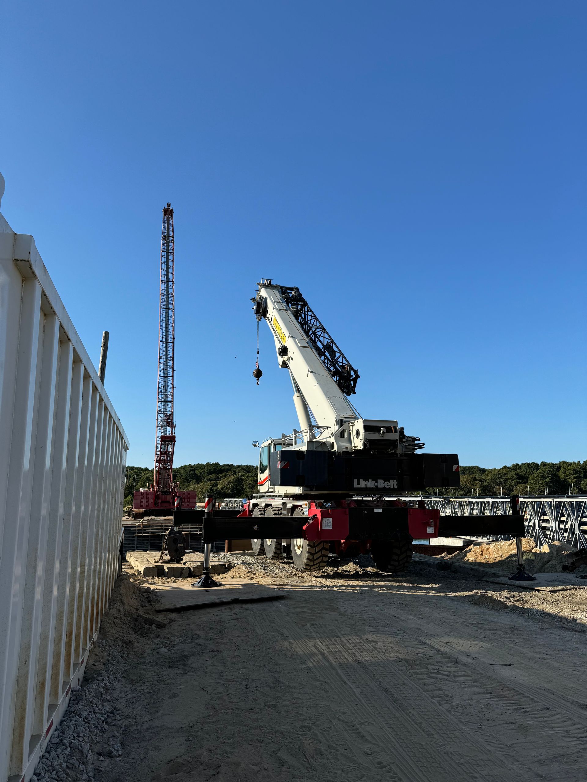 A large yellow tower crane rises next to a multi-story building under construction against a bright blue sky.