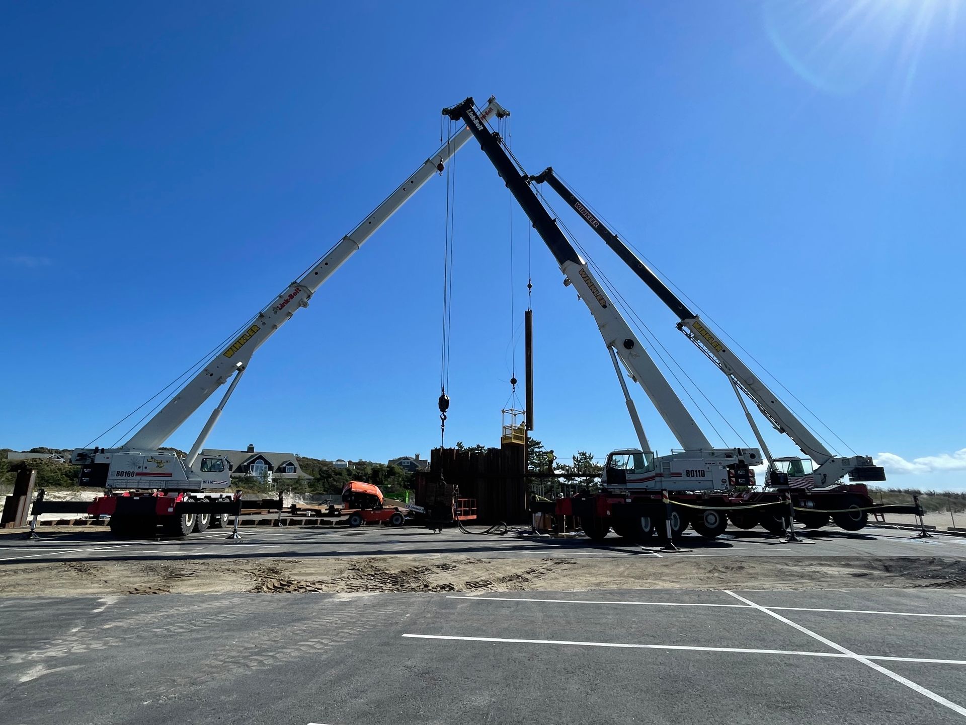 A large mobile crane parked on a dirt construction site at sunset with its boom extended upward.
