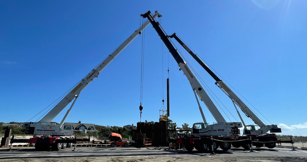 A large mobile crane parked on a dirt construction site at sunset with its boom extended upward.