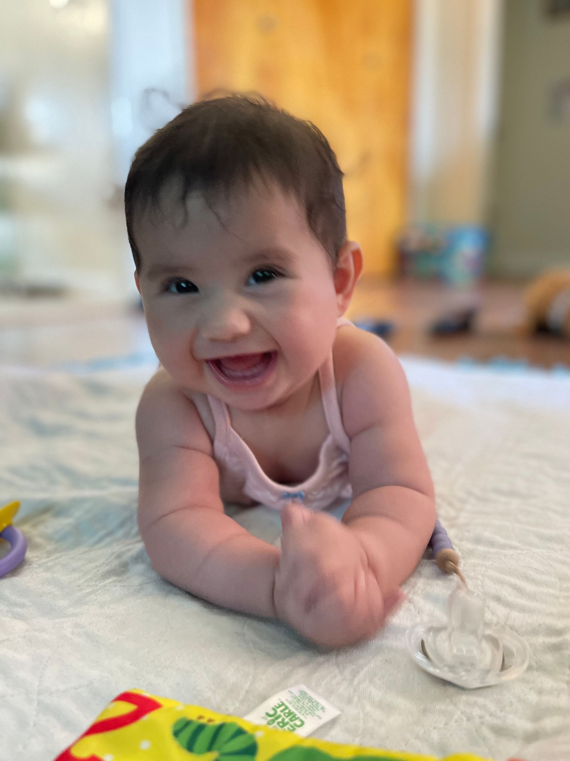 Baby smiling, lying on a patterned blanket, indoors.
