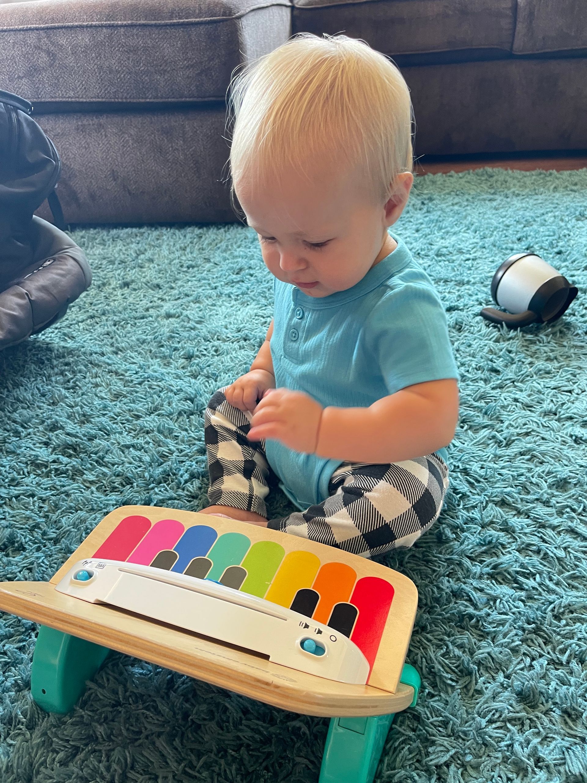 Baby sits on blue rug, playing a xylophone toy with colorful keys.