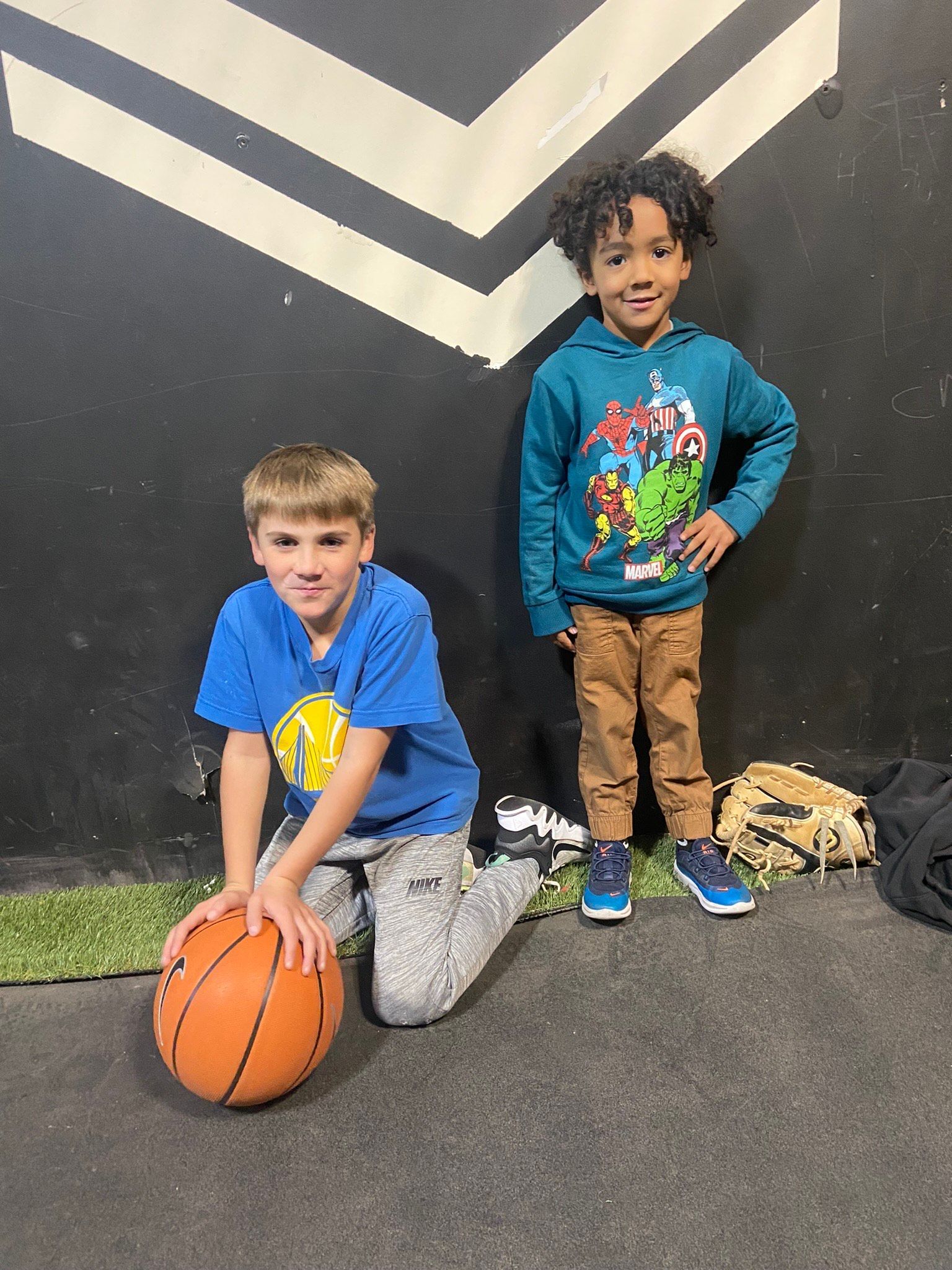 Two young boys are kneeling next to each other with a basketball.