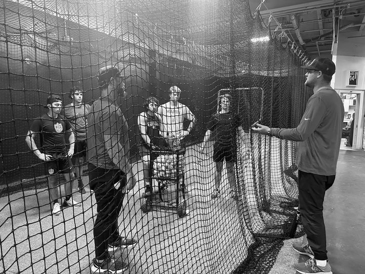 A group of people are standing in front of a baseball net.