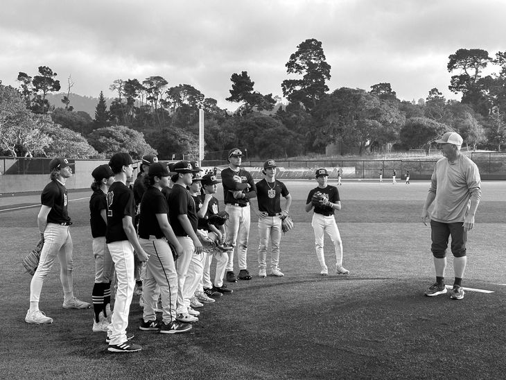 A man is talking to a group of young baseball players on a field.