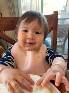 Smiling baby in bib covered in food, sitting at a wooden table.