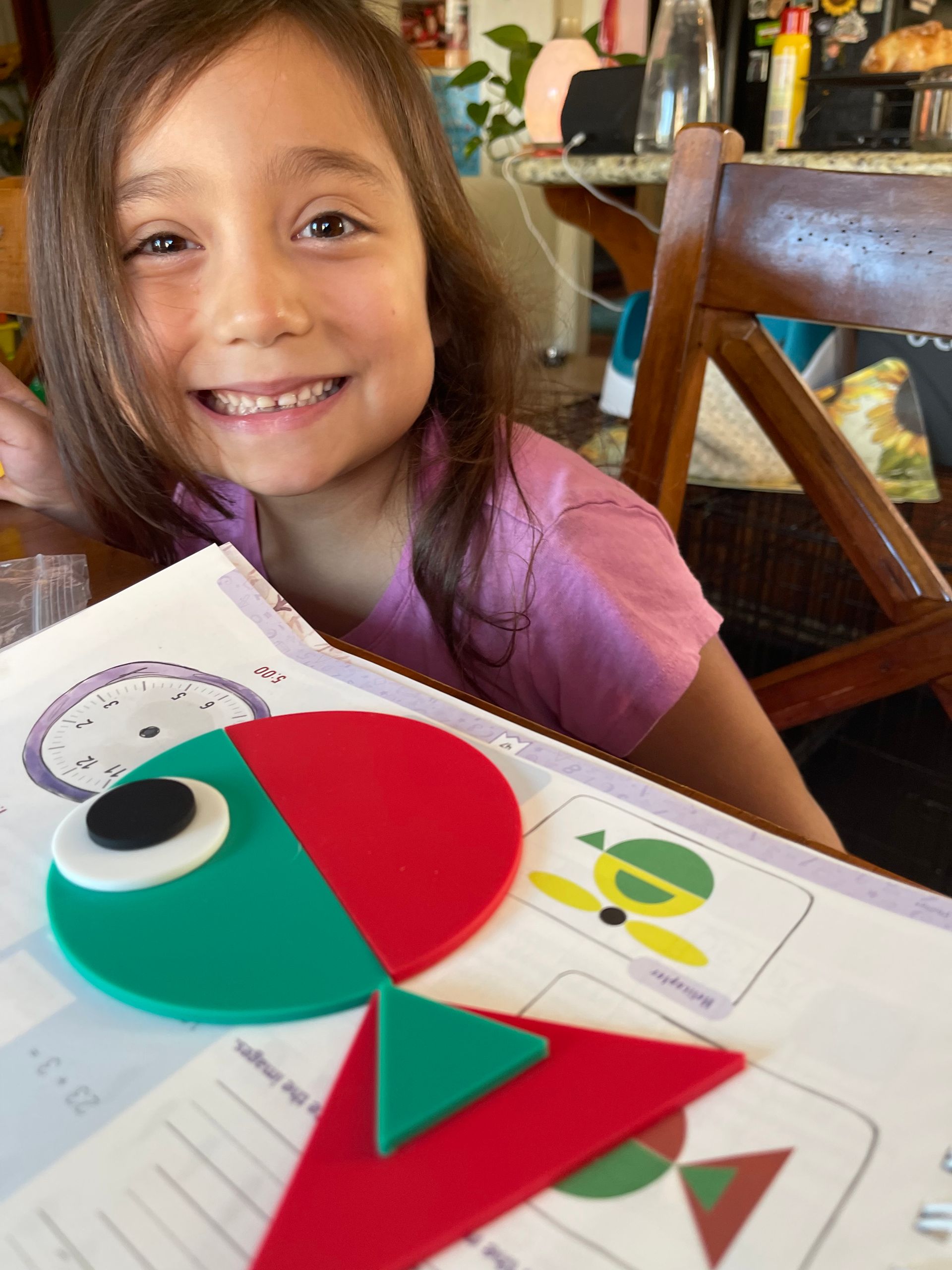 Young girl smiles at the camera, working with colorful geometric shapes.