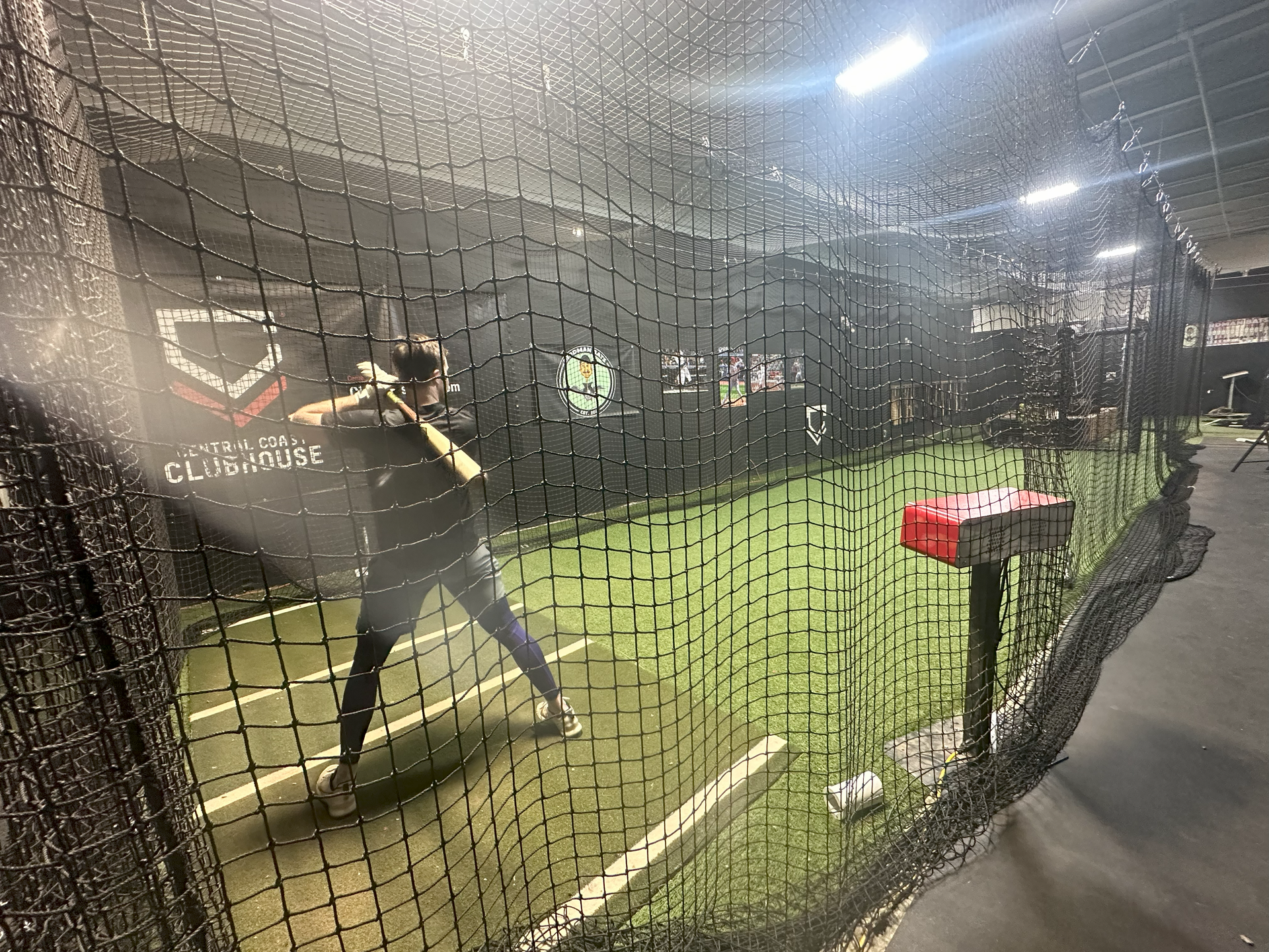 A person is swinging a bat at a baseball in a batting cage.