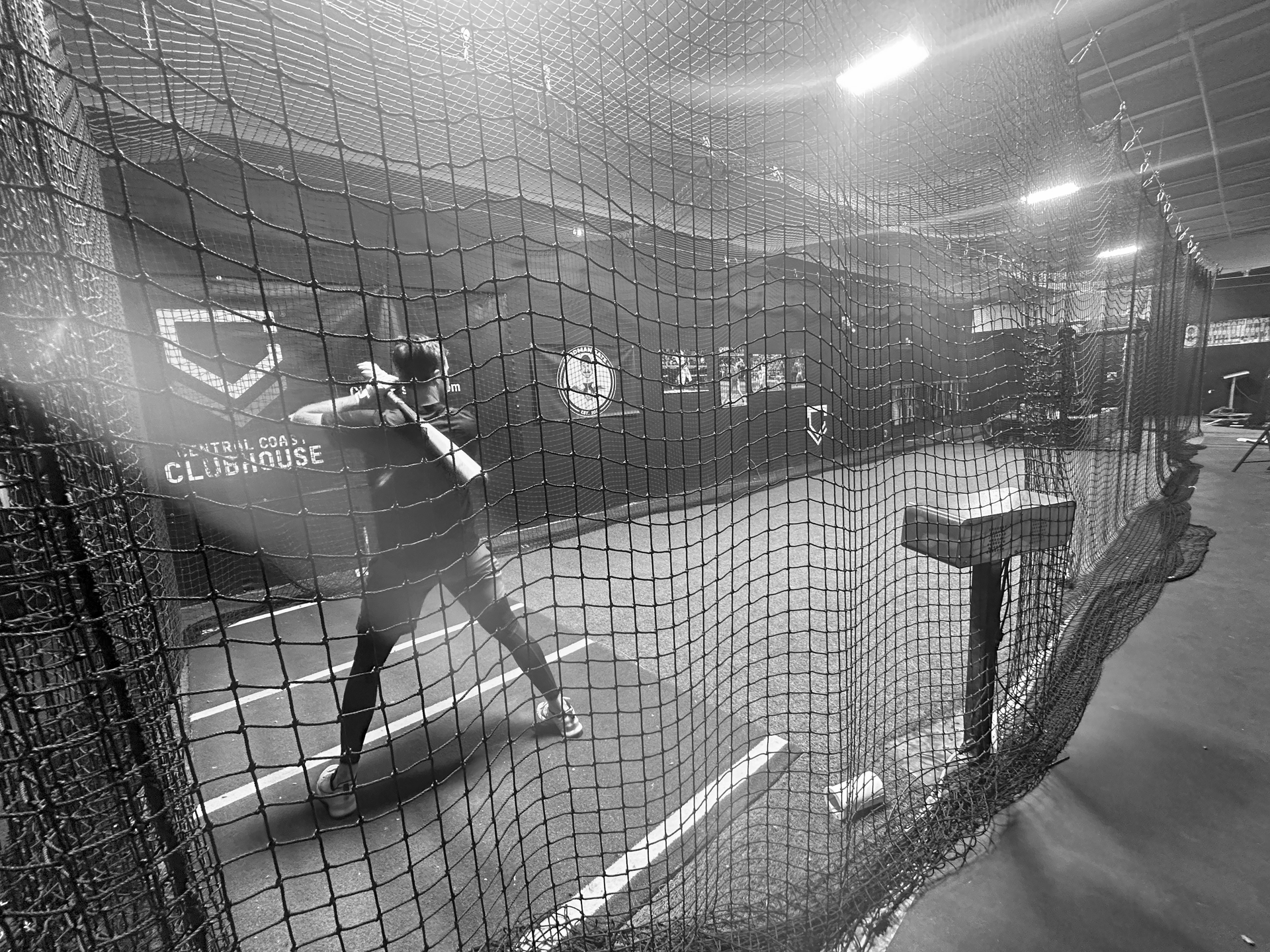 A person is swinging a bat at a baseball in a black and white photo.