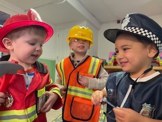 Three children in costumes: firefighter, construction worker, and police officer, smiling.