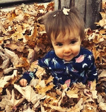 A young child smiles while sitting in a pile of fall leaves.