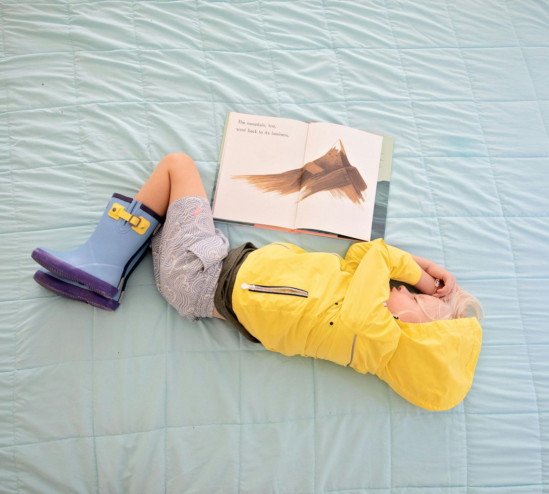 Baby playing a colorful wooden xylophone on a blue rug. He's wearing a blue shirt and patterned pants.