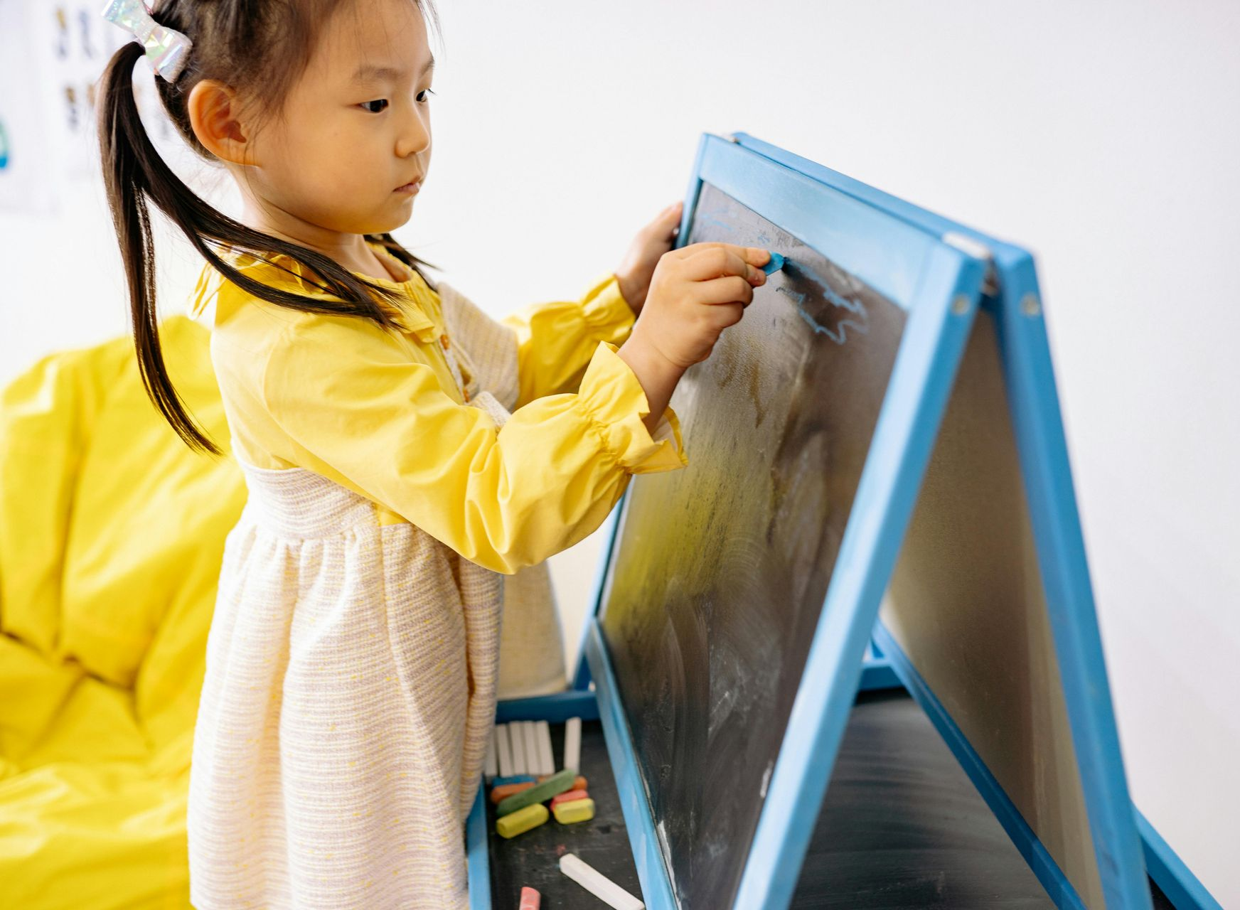 Baby smiles, lying on stomach, hands clasped, wearing a tank top on a light-colored surface with toys.