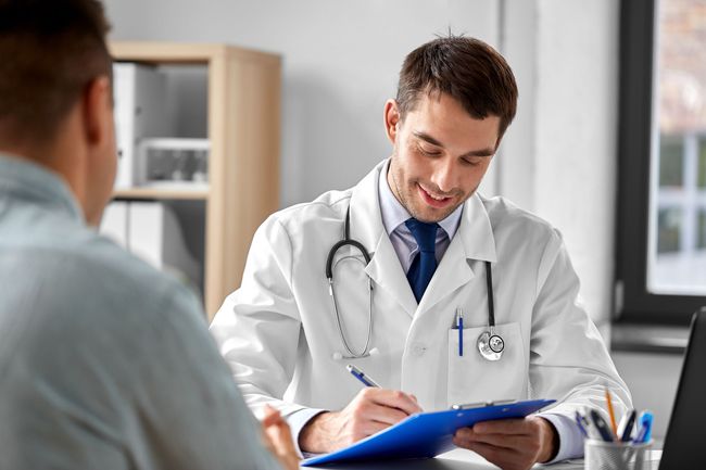 Doctor with clipboard talking to male patient at medical office