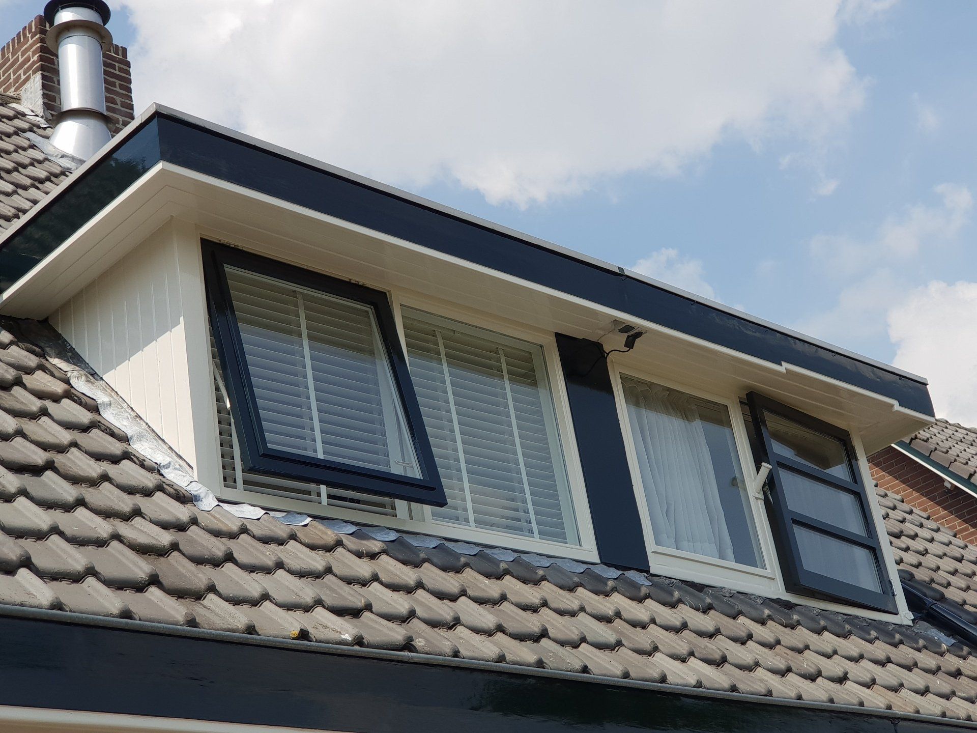 Dakkapel op een dak met open en gesloten ramen. Witte gevelbekleding, donkere randen en dakpannen.