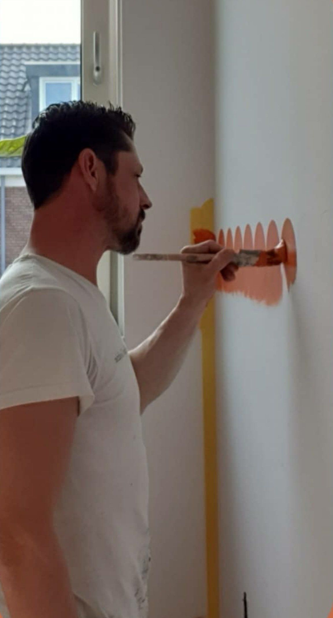 Stefan Godrie schildert oranje lambrisering op een witte muur met een kwast.