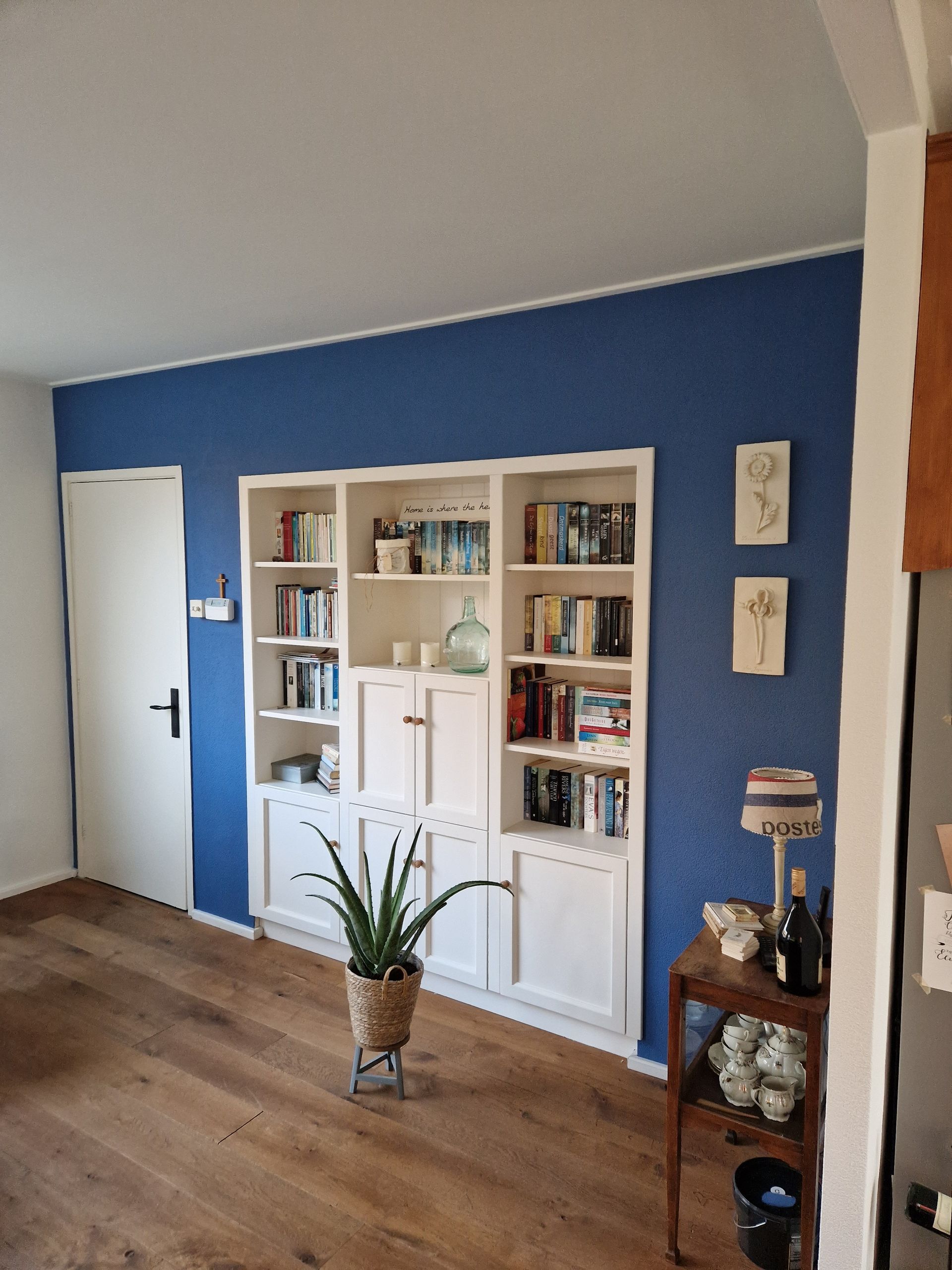 Een witte boekenkast tegen een blauwe gesauste muur in een kamer met een houten vloer, een geschilderde deur.