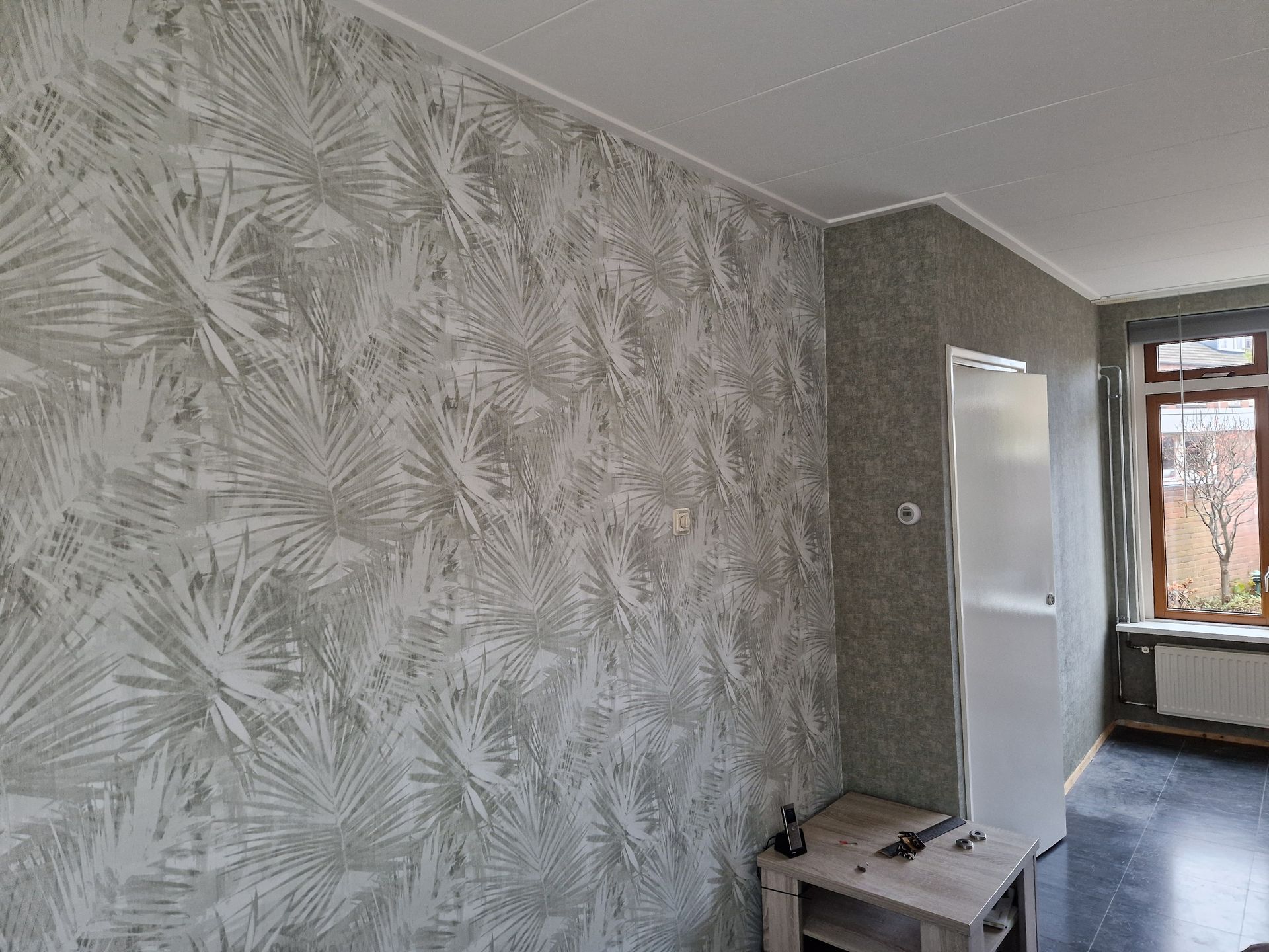 Resultaat van behang met palmbladerenmotief, witte deur en raam.