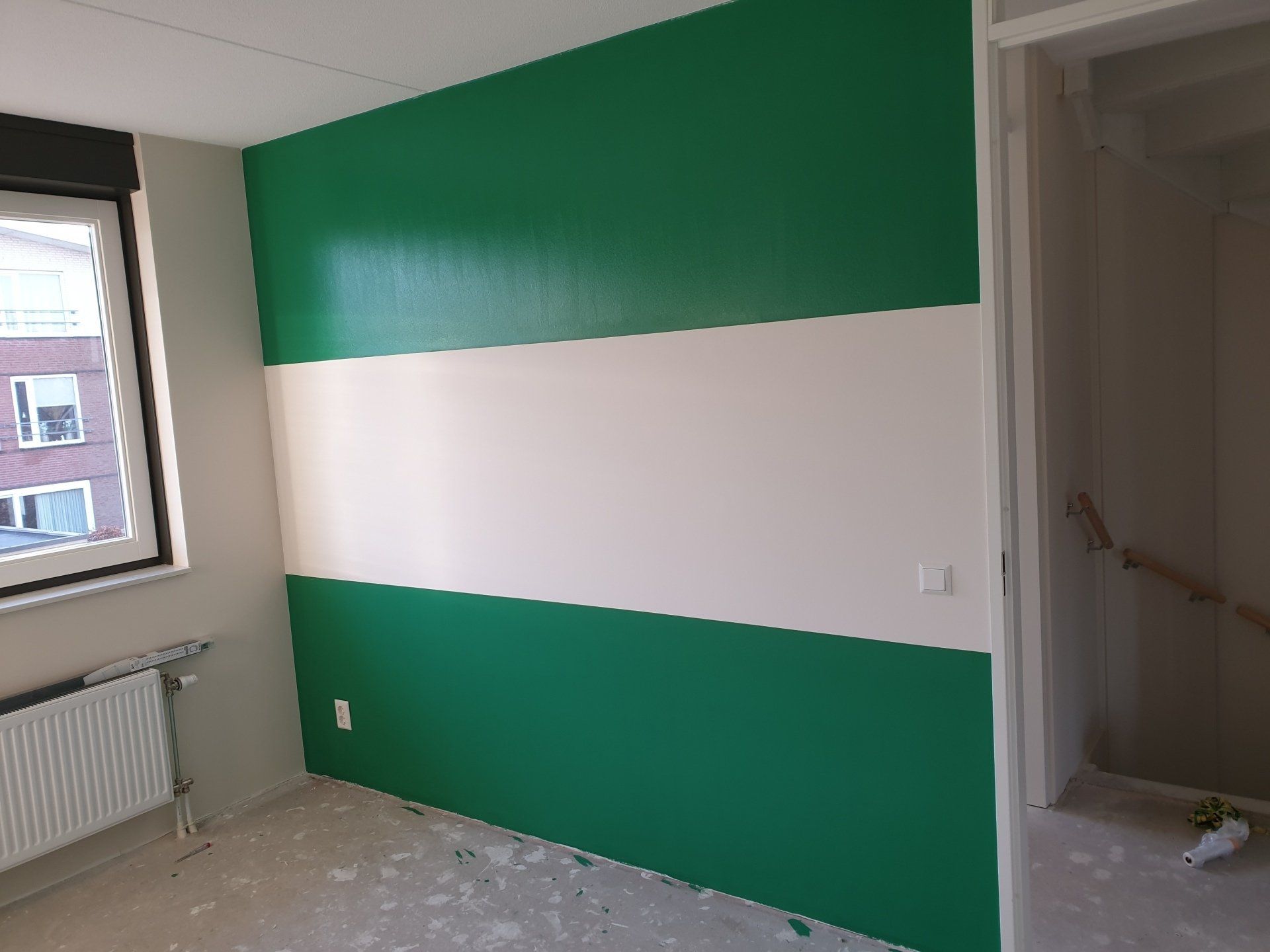 Groen-wit gestreepte ( Rotterdamvlag) muur in een kamer met een raam en een deur.