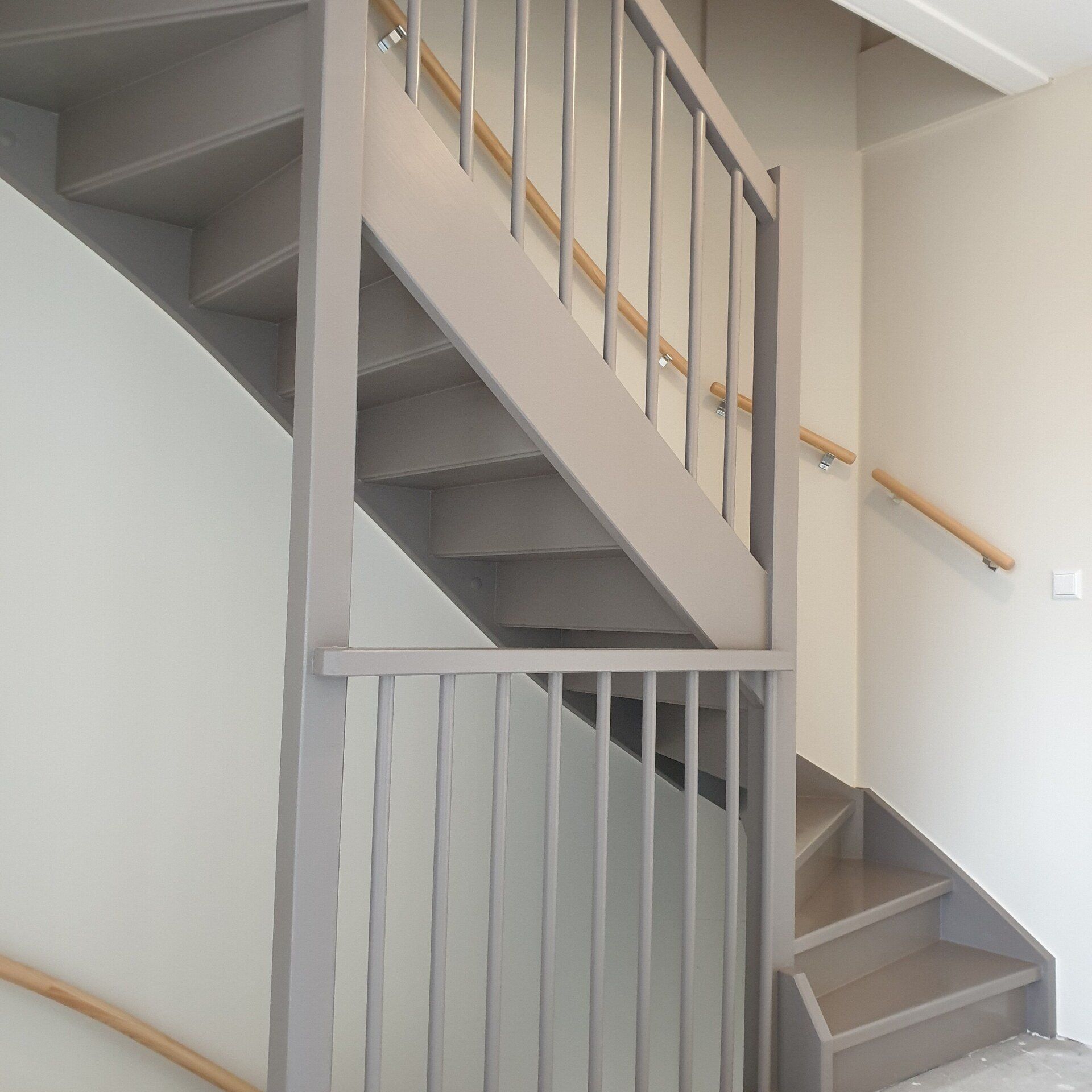 Grijs geschilderde trap met houten leuningen en balustrades.