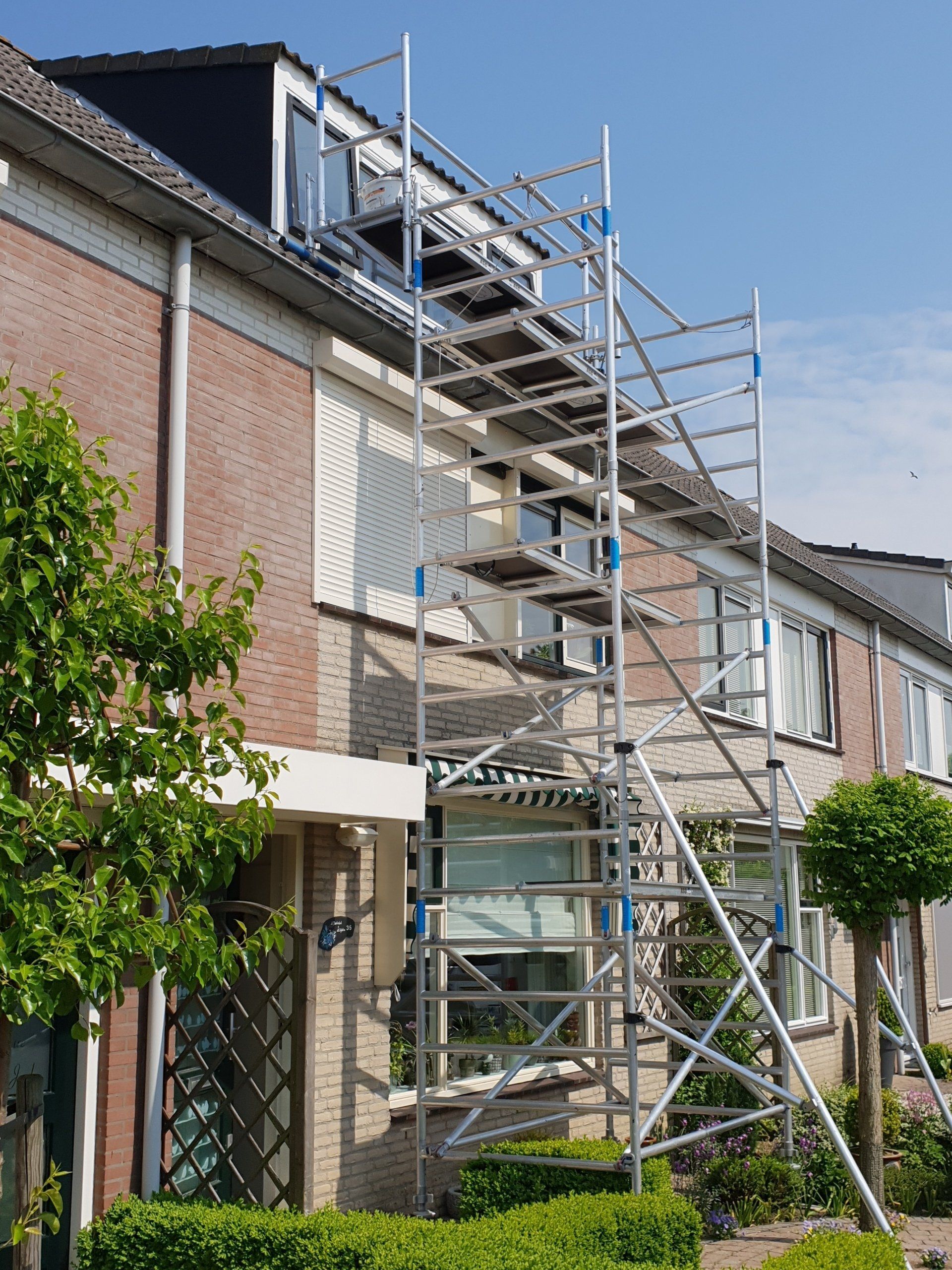 Steigers opgetrokken naast een bakstenen huis om toegang te krijgen tot ramen van een dakkapel, voor schilderwerkzaamheden.