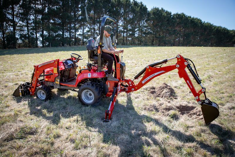 Orange tractor in a field, under a blue sky, with a person driving. Dead trees in the background.