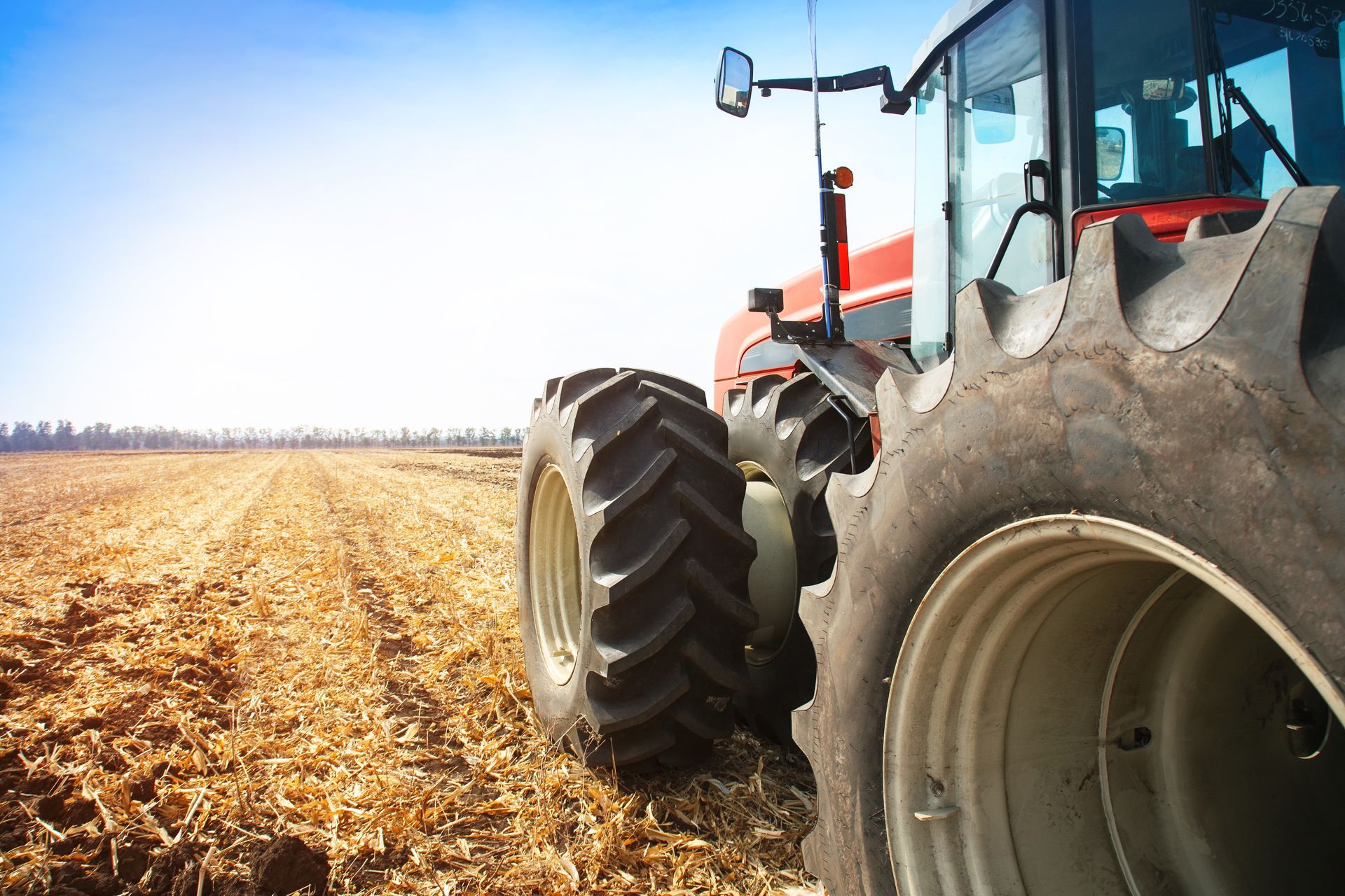 Orange tractor in a field, under a blue sky, with a person driving. Dead trees in the background.