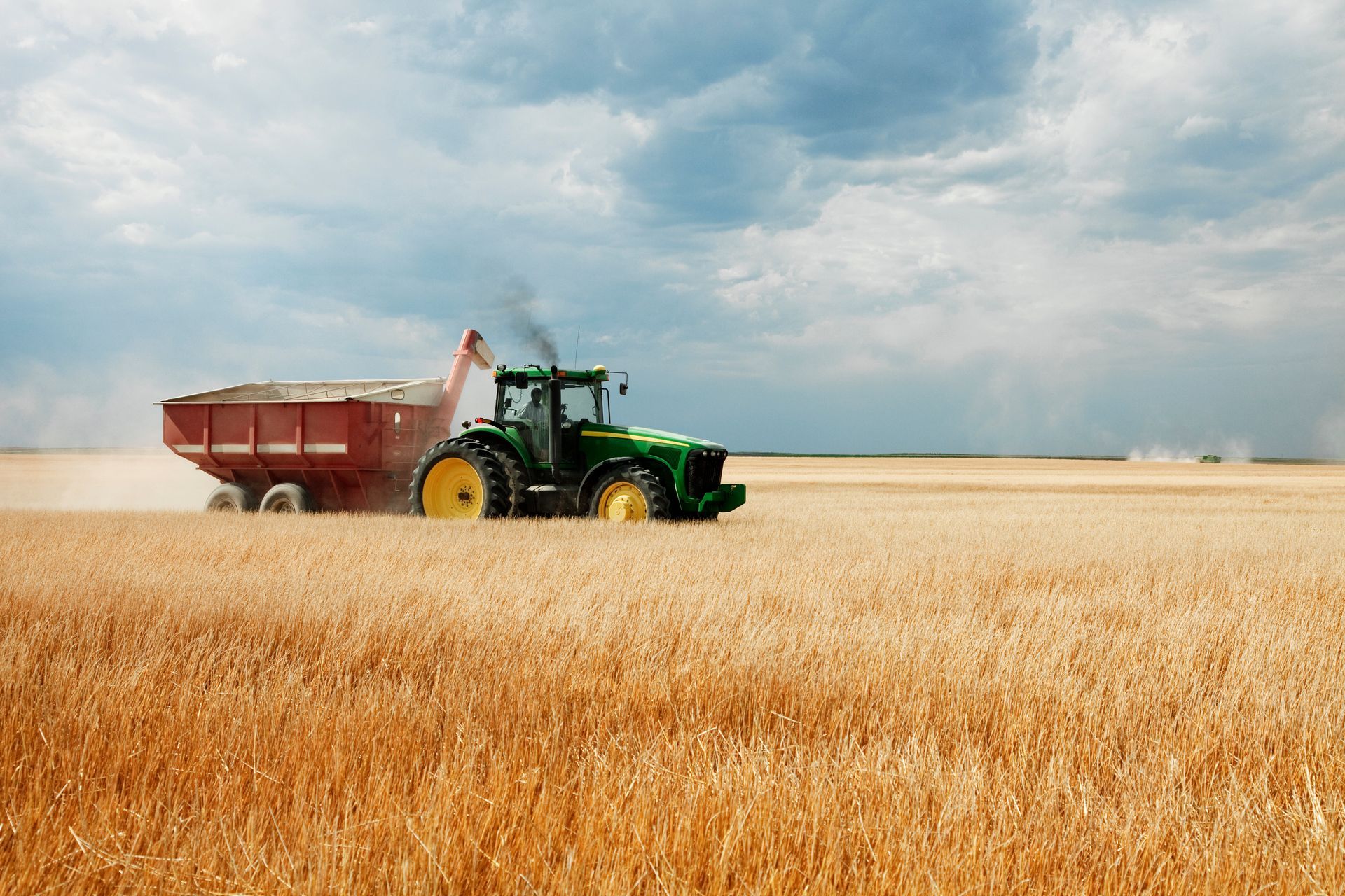 Red tractor mowing tall grass in a field under a cloudy sky.