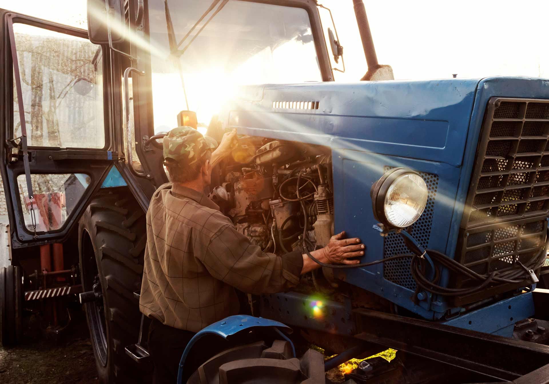 A mechanic performs farm equipment repairs and servicing on a blue tractor.