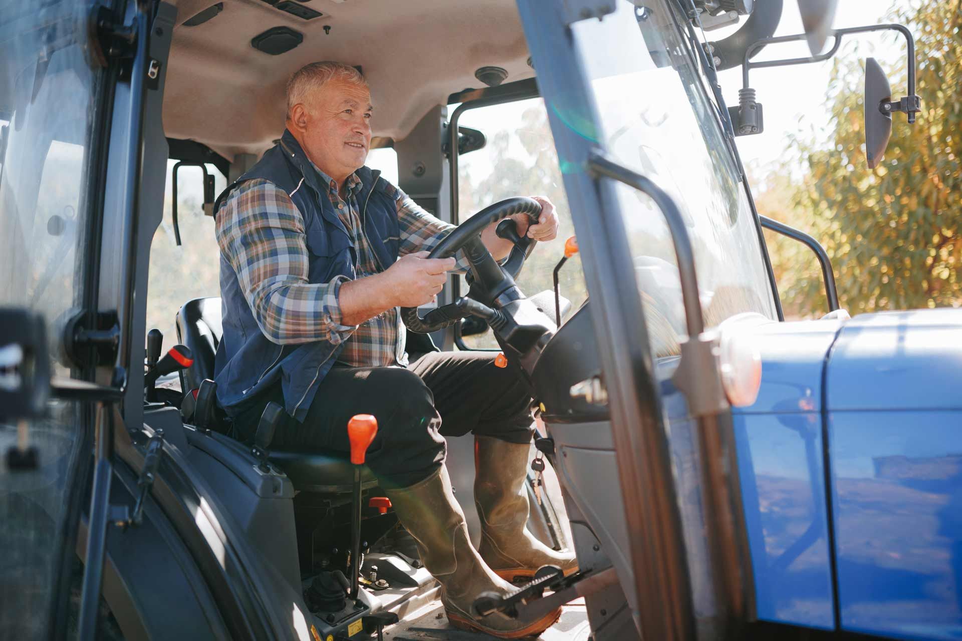 A seasoned farmer at the wheel of a tractor in a field.