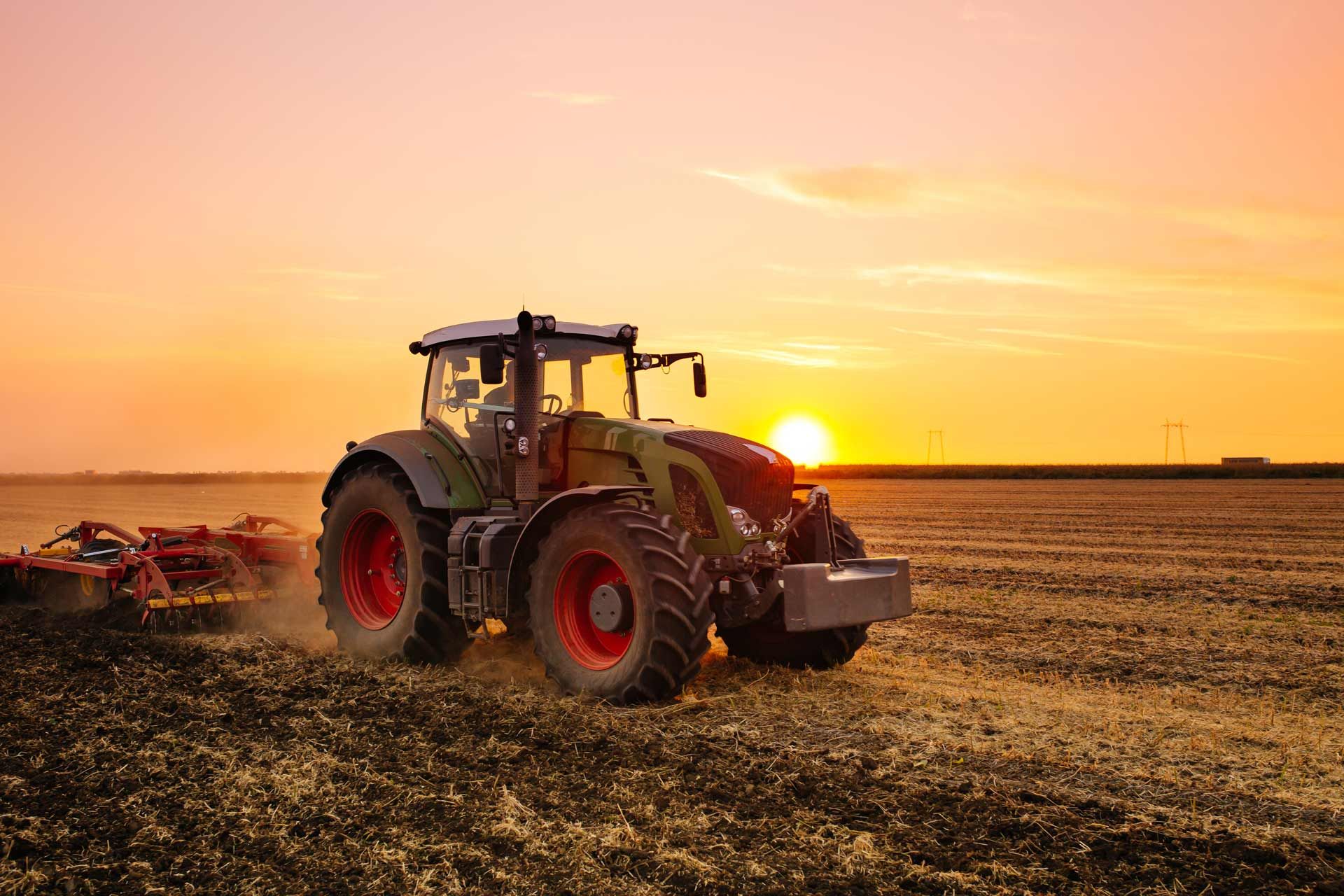 A farm tractor on the barley field by the sunset.