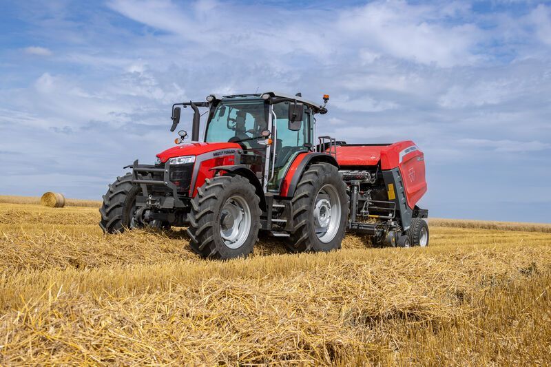 Row of large red tractors parked on grass beside a paved road.